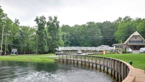 A lakeside view with a wooden dock, a restaurant with outdoor seating, and a building with a star on the roof. - Sun Valley Camping and RV Resort (Narvon)