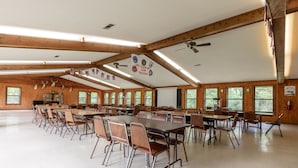 A large hall with multiple tables and chairs, wooden beams, and flags. - Cherokee Landing Campground (Saulsbury)