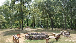 A campsite with a circular fire pit surrounded by wooden benches, a playground with a slide, and dense trees in the background. - Cherokee Landing Campground (Saulsbury)