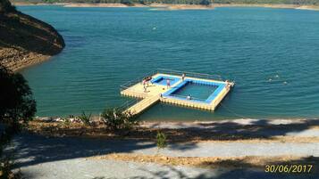 A floating platform with a pool in the middle of a lake, surrounded by a rocky shoreline.