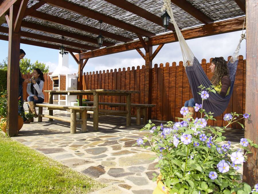Un patio al aire libre con una pérgola de madera, suelo de piedra y una hamaca.