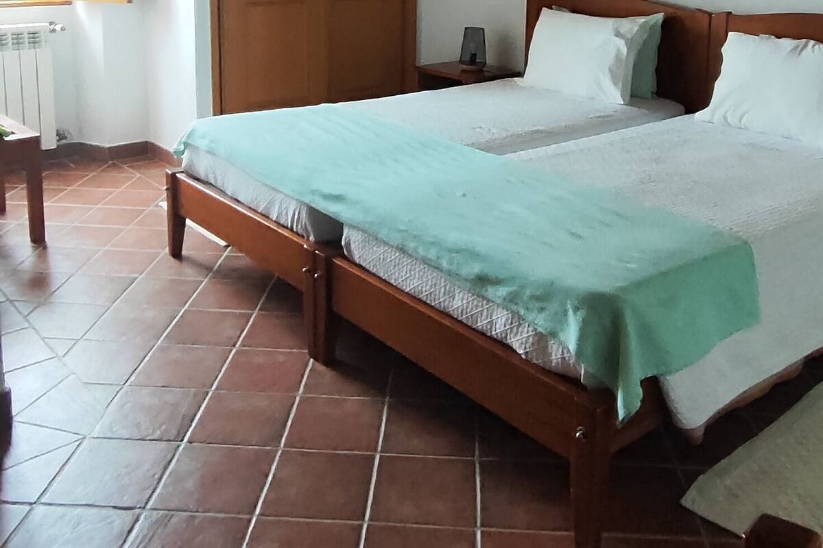 A bedroom with a wooden bed, a nightstand, a window with wooden shutters, and a door.
