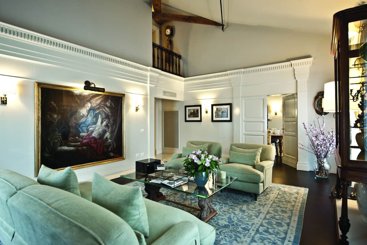 A spacious living room with a large painting, a green sofa set, a coffee table, and a blue patterned rug.