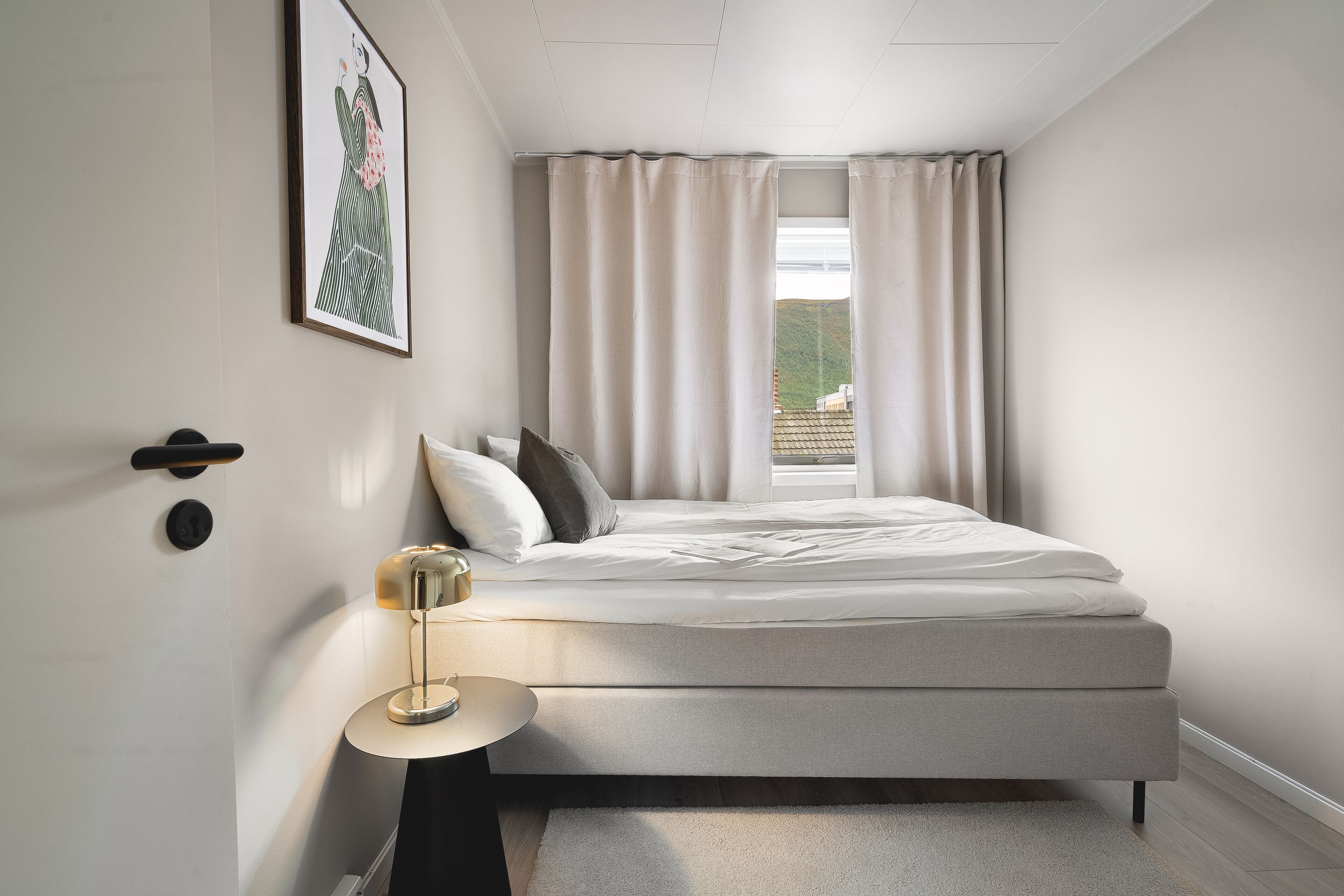 A modern bedroom with a bed, a bedside table, a lamp, and a window with curtains.