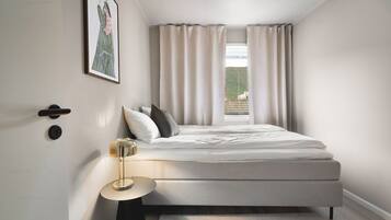 A modern bedroom with a bed, a bedside table, a lamp, and a window with curtains.