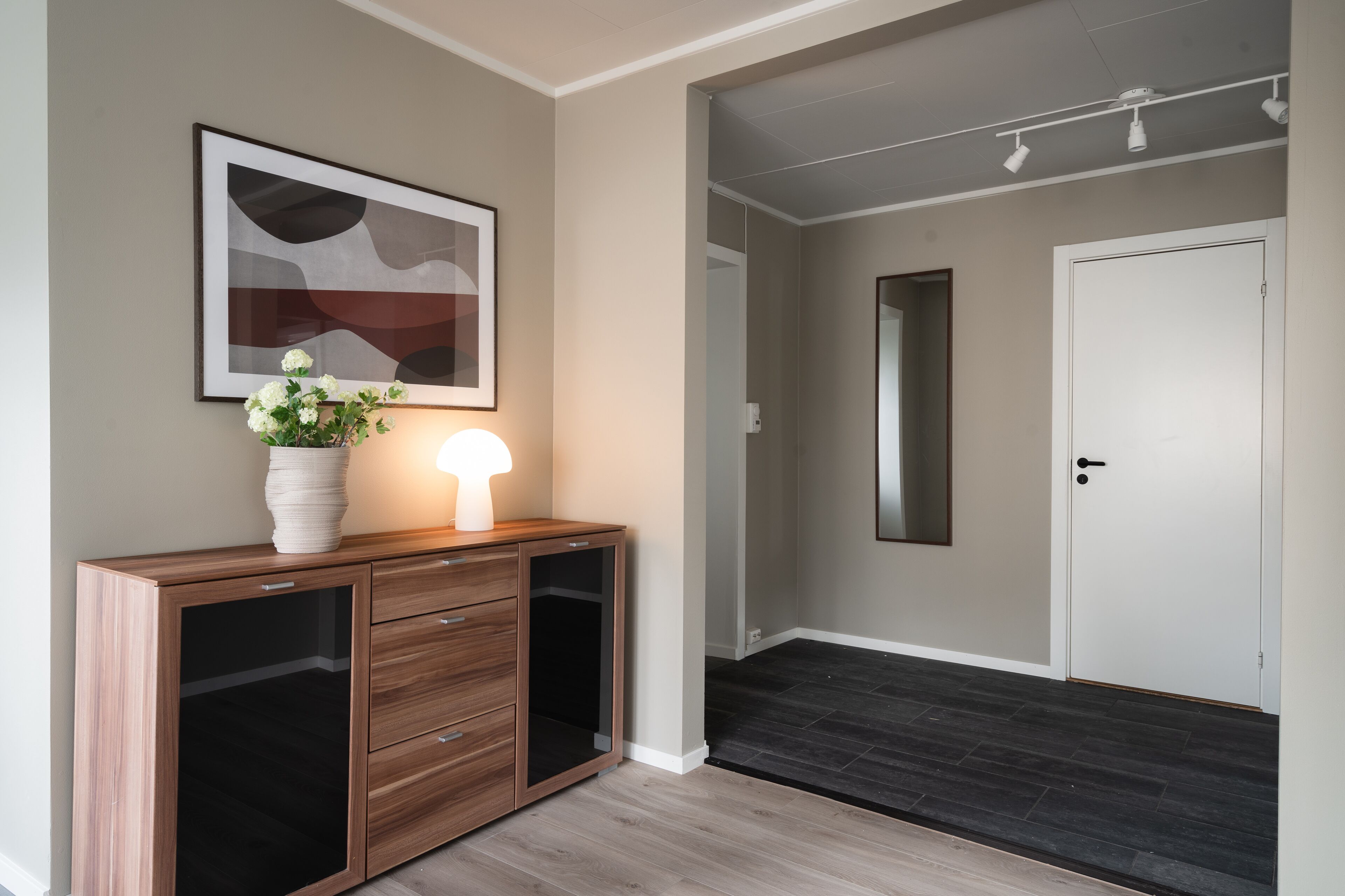 A hallway with a wooden console table, a framed abstract painting, and a potted plant.