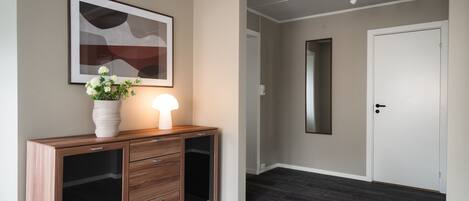 A hallway with a wooden console table, a framed abstract painting, and a potted plant.