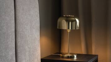 Une lampe moderne posée sur une petite table à côté d’un canapé, avec un mur sombre à texture et un rideau en arrière-plan.