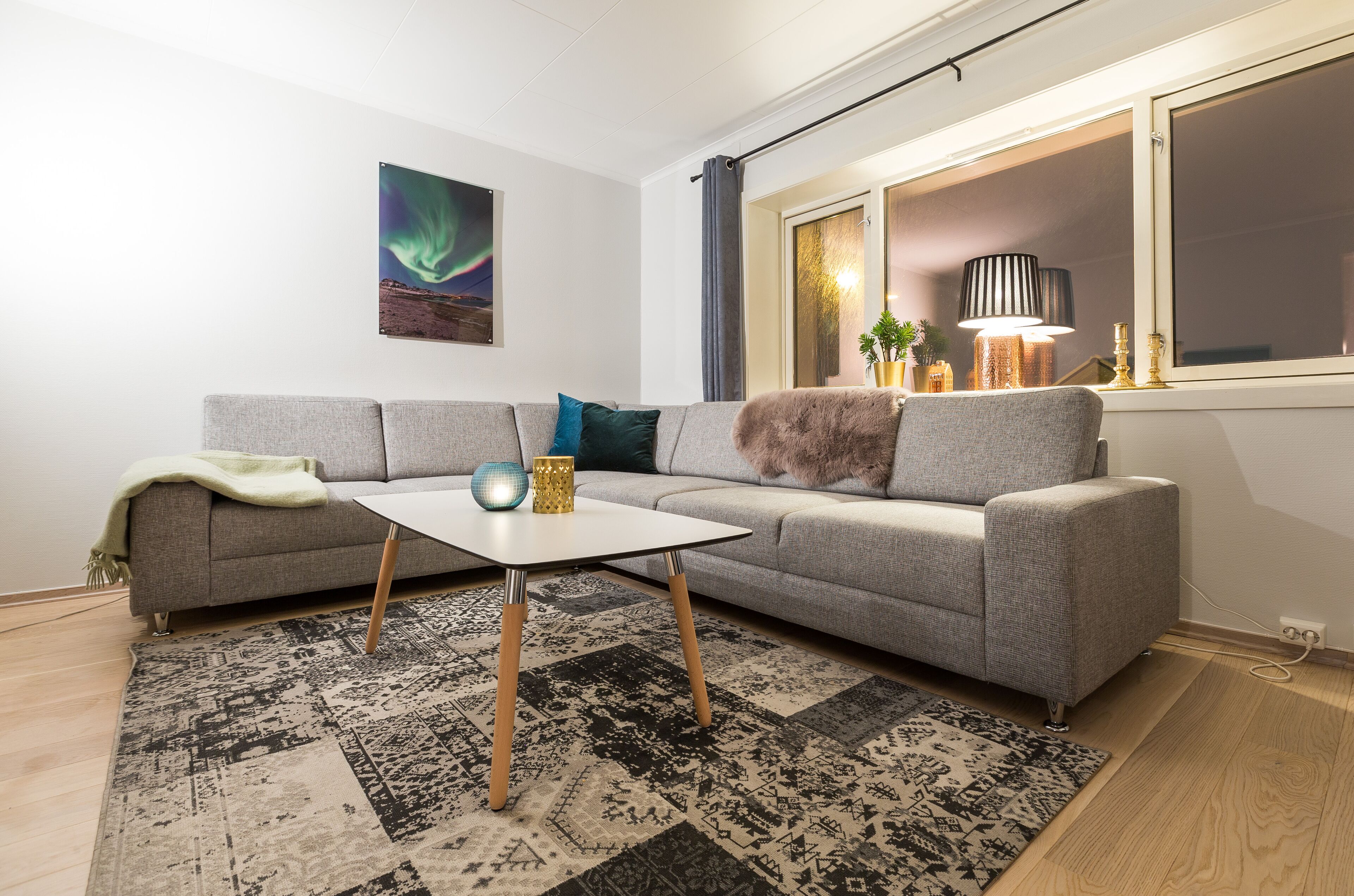 A modern living room with a grey sofa, a white coffee table, and a patterned rug.