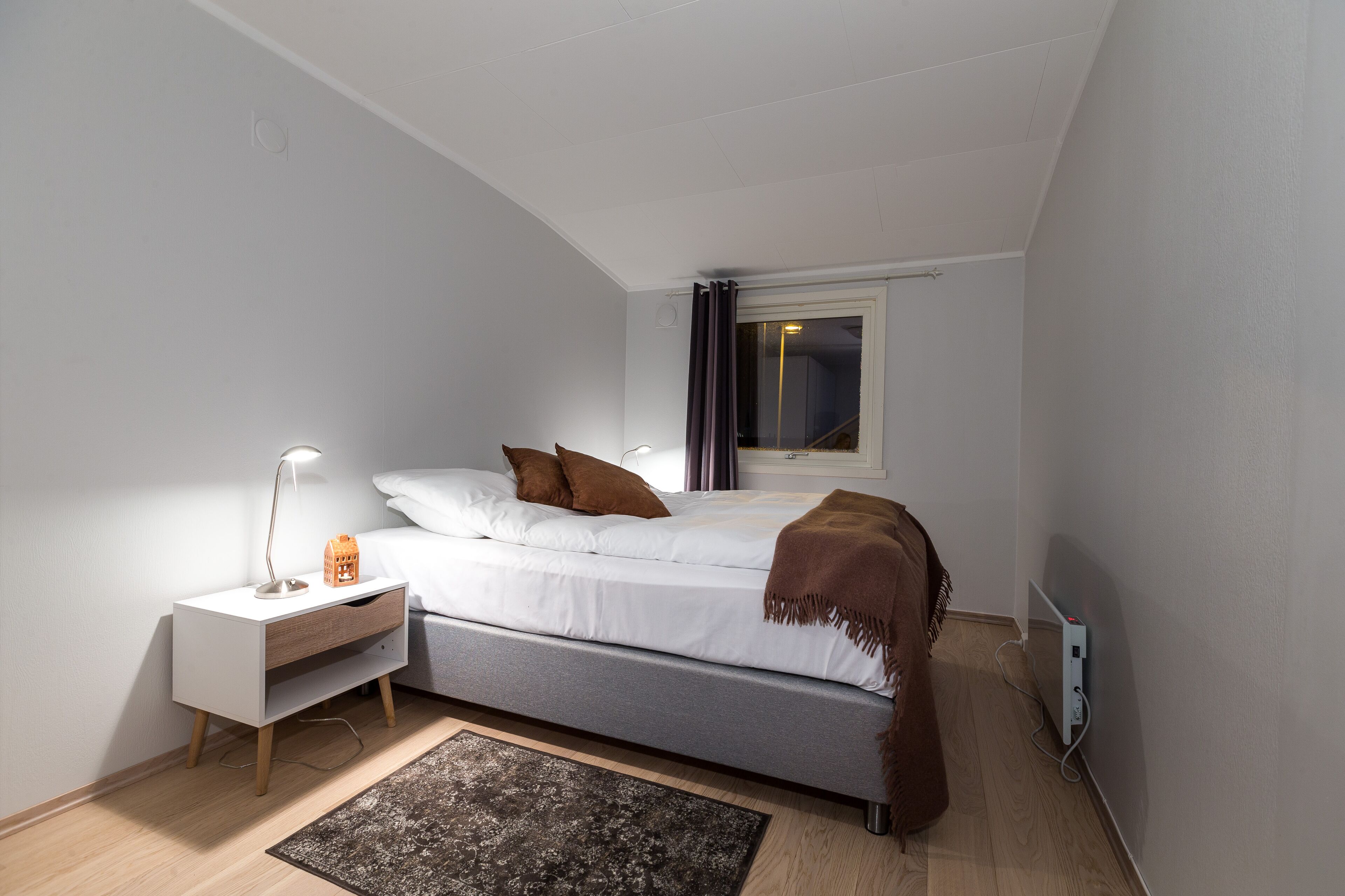 A bedroom with a bed, bedside table, lamp, and a window with curtains.