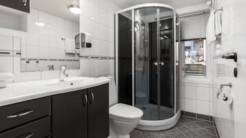 Une salle de bain moderne avec un lavabo blanc, des meubles sombres, des toilettes blanches et une douche à parois de verre.
