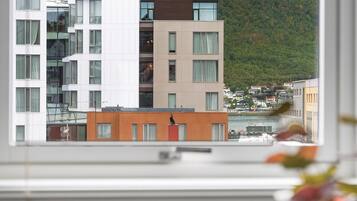 Vista desde una ventana de un edificio con arquitectura moderna, con fachadas en tonos blanco y marrón, y un paisaje montañoso al fondo.