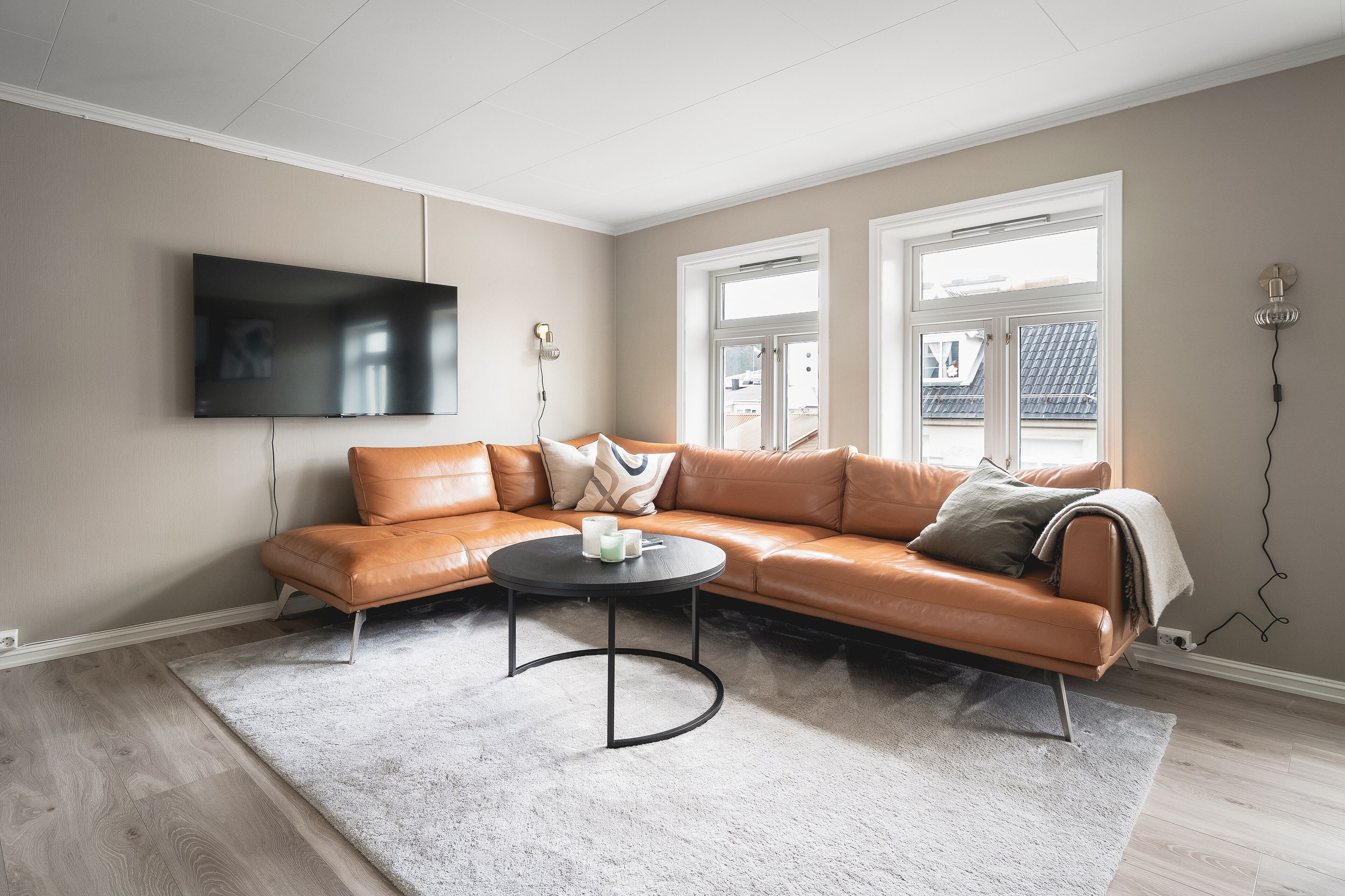 A living room with a brown leather sofa, a round coffee table, and a flat-screen TV mounted on the wall.