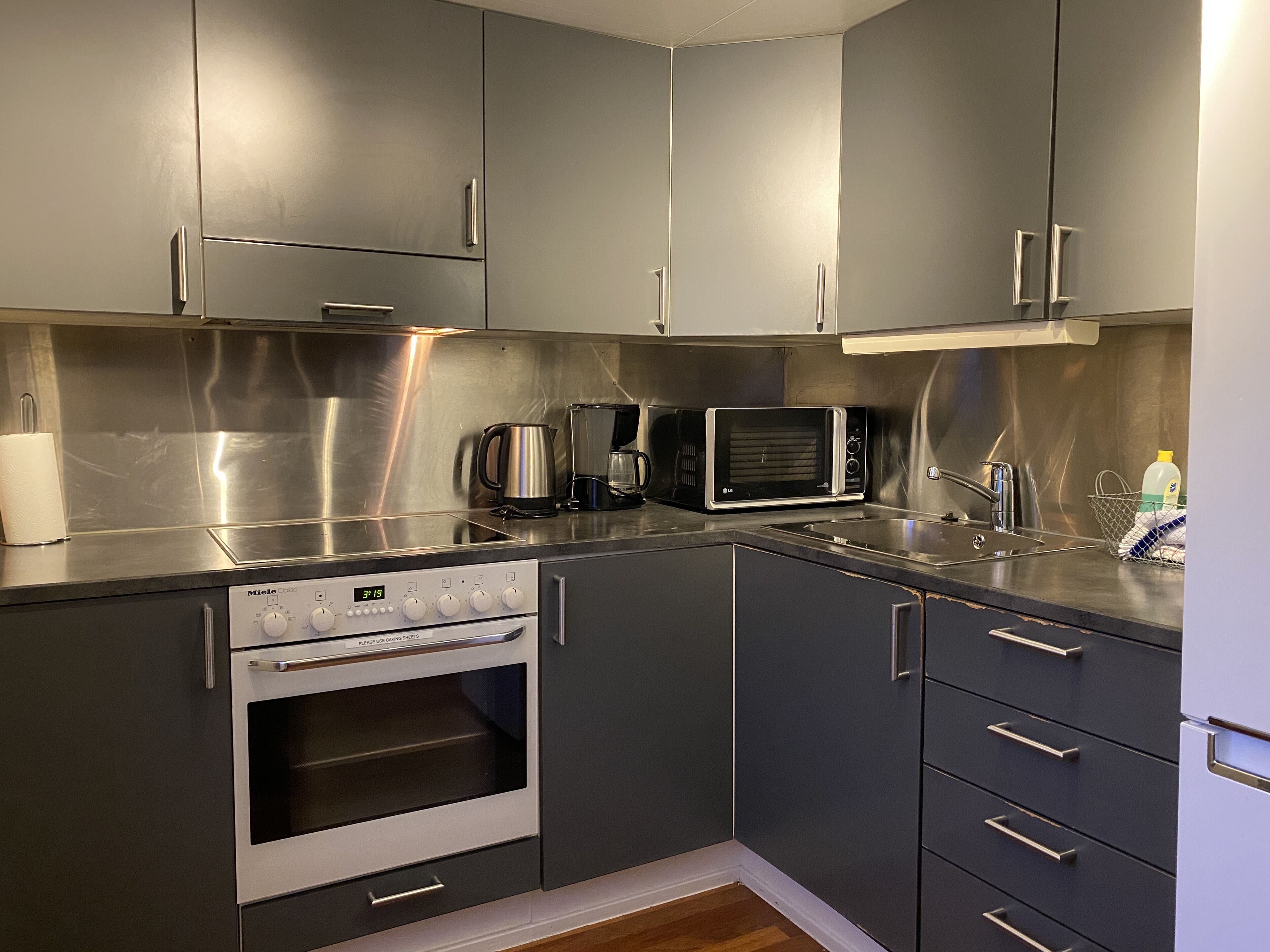 A modern kitchen with stainless steel appliances, grey cabinets, and a built-in oven.