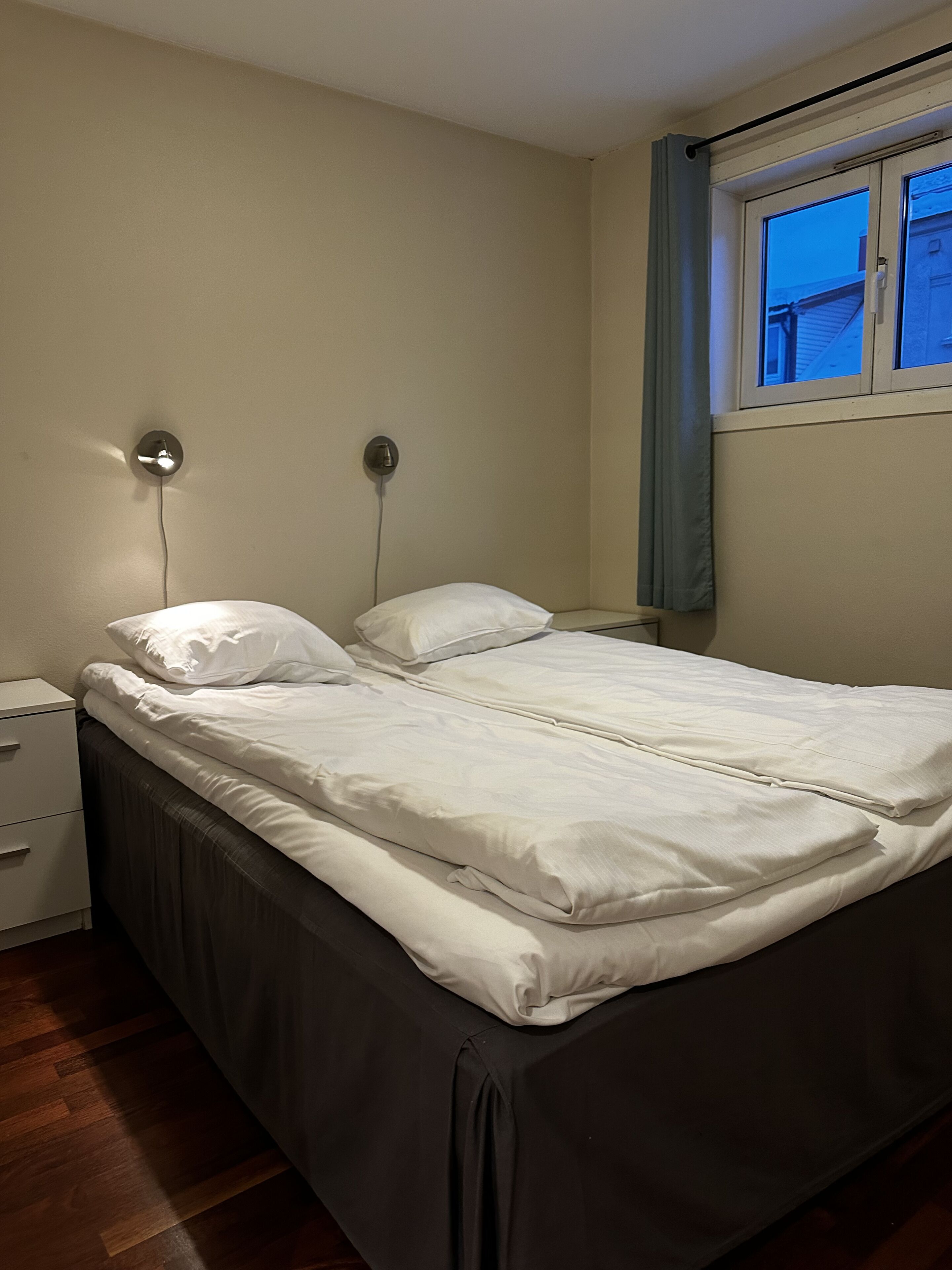 Un dormitorio con una cama, mesitas de noche y un ventanal con cortinas.