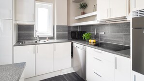 Une cuisine moderne avec des meubles blancs, un lave-vaisselle, un plan de travail noir et une fenêtre.