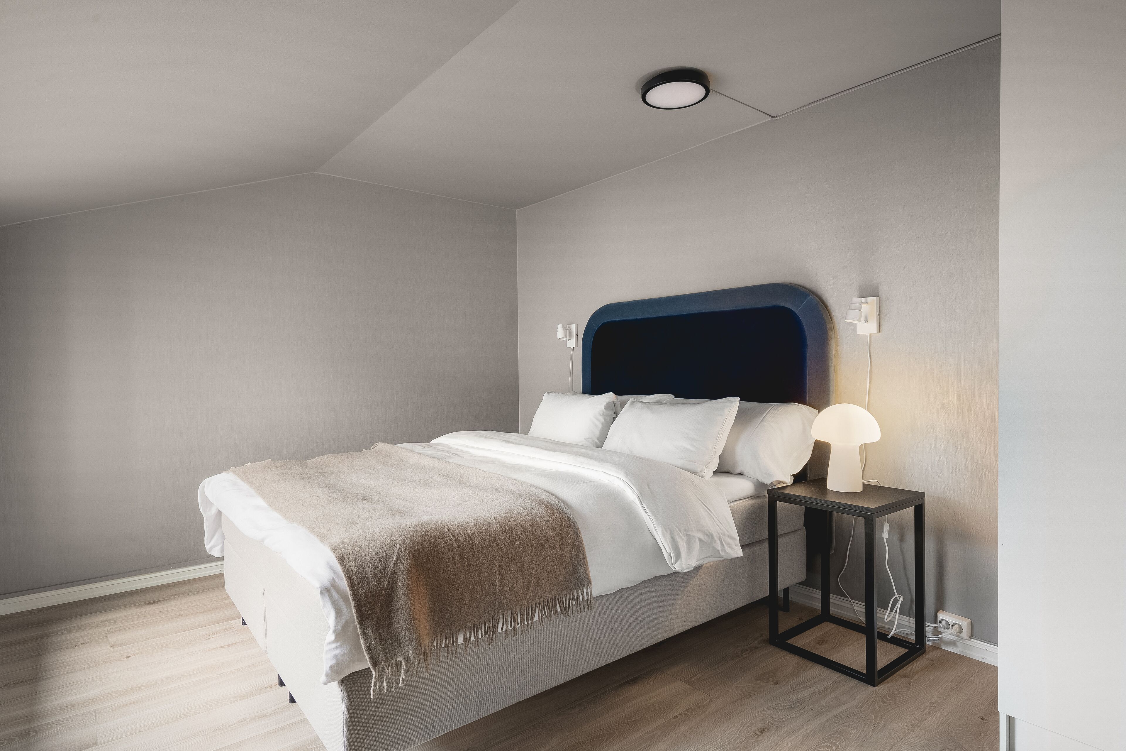 A modern bedroom with a bed, bedside table, and a lamp.