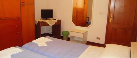 A bedroom with two beds, a desk with a computer, a mirror, and a wardrobe.