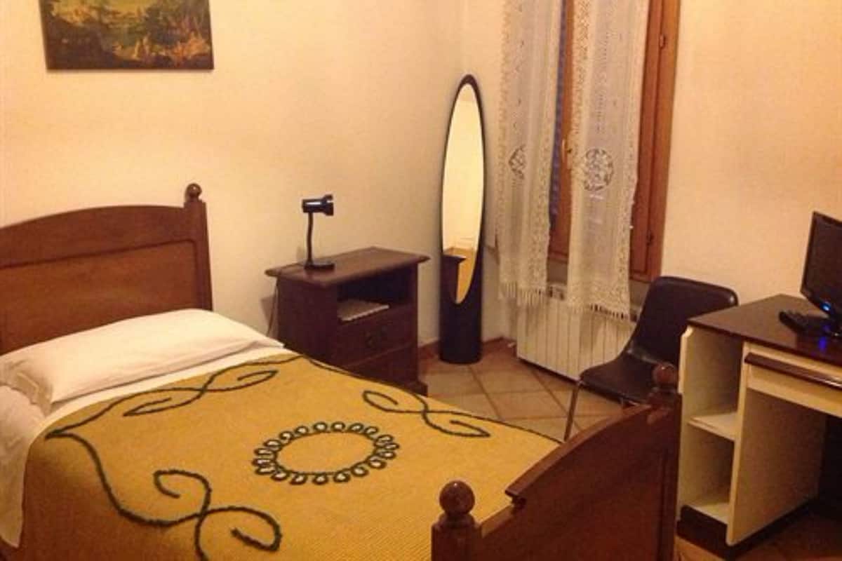 A hotel room with a bed, a desk with a computer, a chair, a mirror, and a painting on the wall.