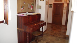 A hallway with a wooden piano, a stone floor, and a door at the end.