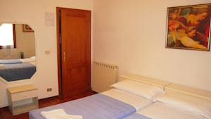 A hotel room with two beds, a wooden door, a radiator, a dresser, a mirror, and a painting on the wall.