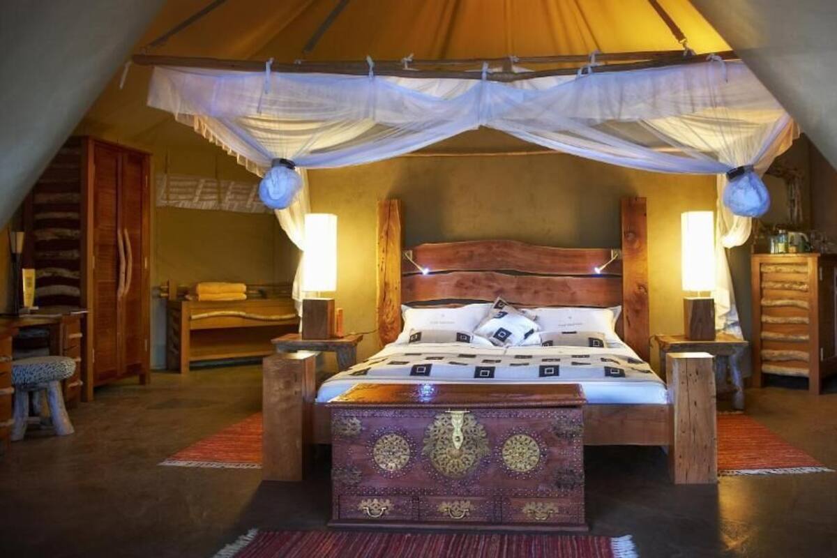 A cozy, tent-style bedroom with a wooden bed, two bedside lamps, and a decorative chest of drawers.