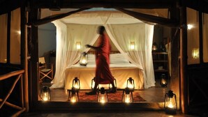 A room with a bed under a canopy, surrounded by lanterns, and a person in a red robe. - Severin Safari Camp (Tsavo)