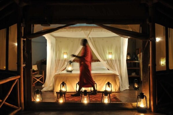 Una habitación con cama bajo un dosel, rodeada de faroles y una persona vestida con una túnica roja.