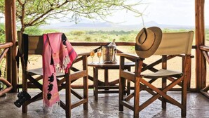 A wooden deck with a table and chairs, a blanket, a hat, and a camera. - Severin Safari Camp (Tsavo)