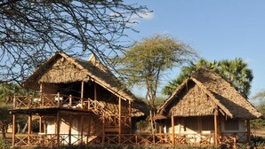 Two thatched-roof huts with wooden railings, surrounded by trees and a clear sky. - Severin Safari Camp (Tsavo)