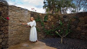 A person in a white dress standing in a stone-walled outdoor area with a small tree and plants. - Severin Safari Camp (Tsavo)