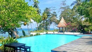 A swimming pool with a thatched-roof structure, surrounded by lush greenery and a view of the sea. - Asana Biak Papua (Biak)