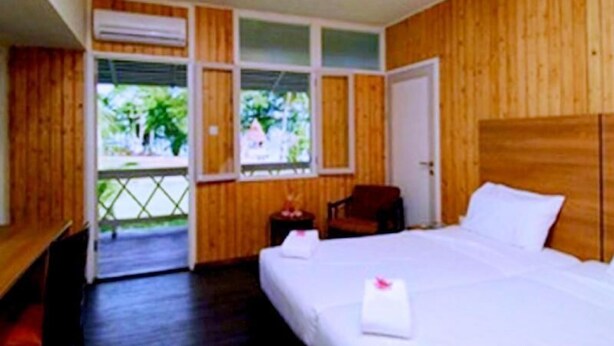 A room with wooden paneling, a bed with white linens, a chair, and a small table. - Asana Biak Papua (Biak)