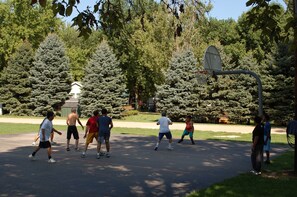 Un terrain de basket entouré d’arbres et un bâtiment à la façade blanche.