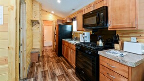 A compact kitchen with wooden cabinets, a black stove, a microwave, and a sink. - O'Connell's RV Campground (Amboy)