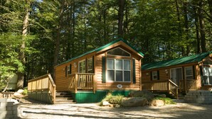 A wooden cabin with a green roof, a porch, and a gravel driveway.