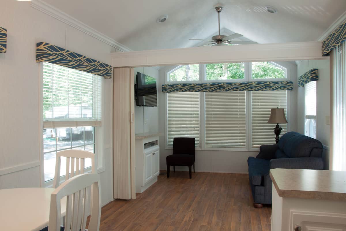 A room with a ceiling fan, a window with blinds, a black chair, a blue couch, and a wooden floor.