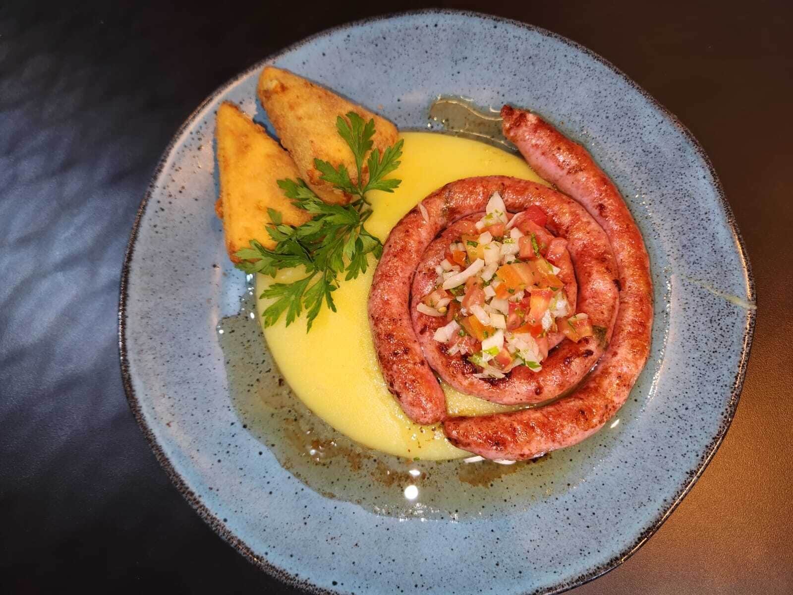 Une assiette avec une saucisse, un accompagnement et une sauce jaune.
