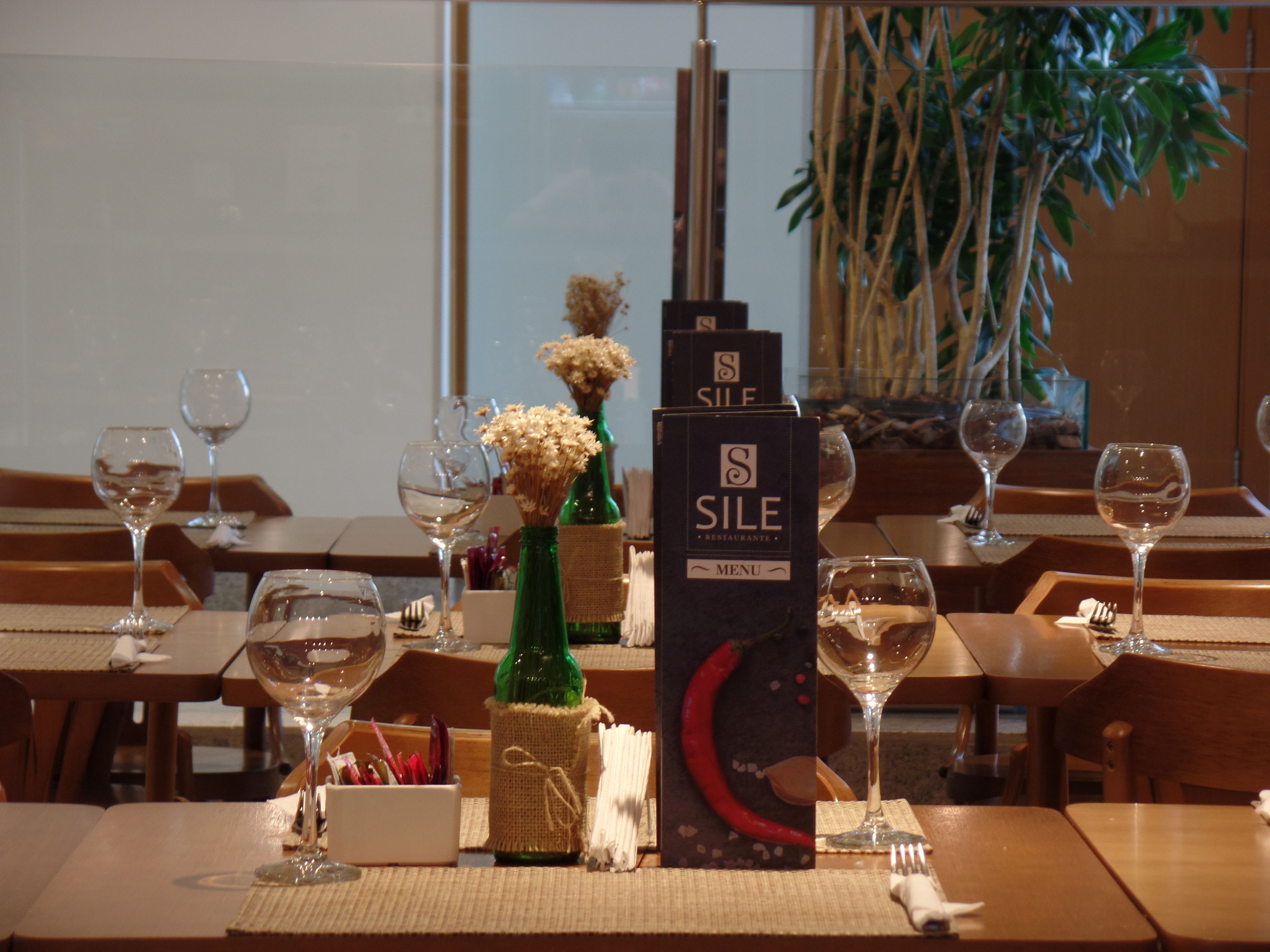 Un ambiente de restaurante con mesas dispuestas para comer, destacando copas de vino, menús y una botella de vino.