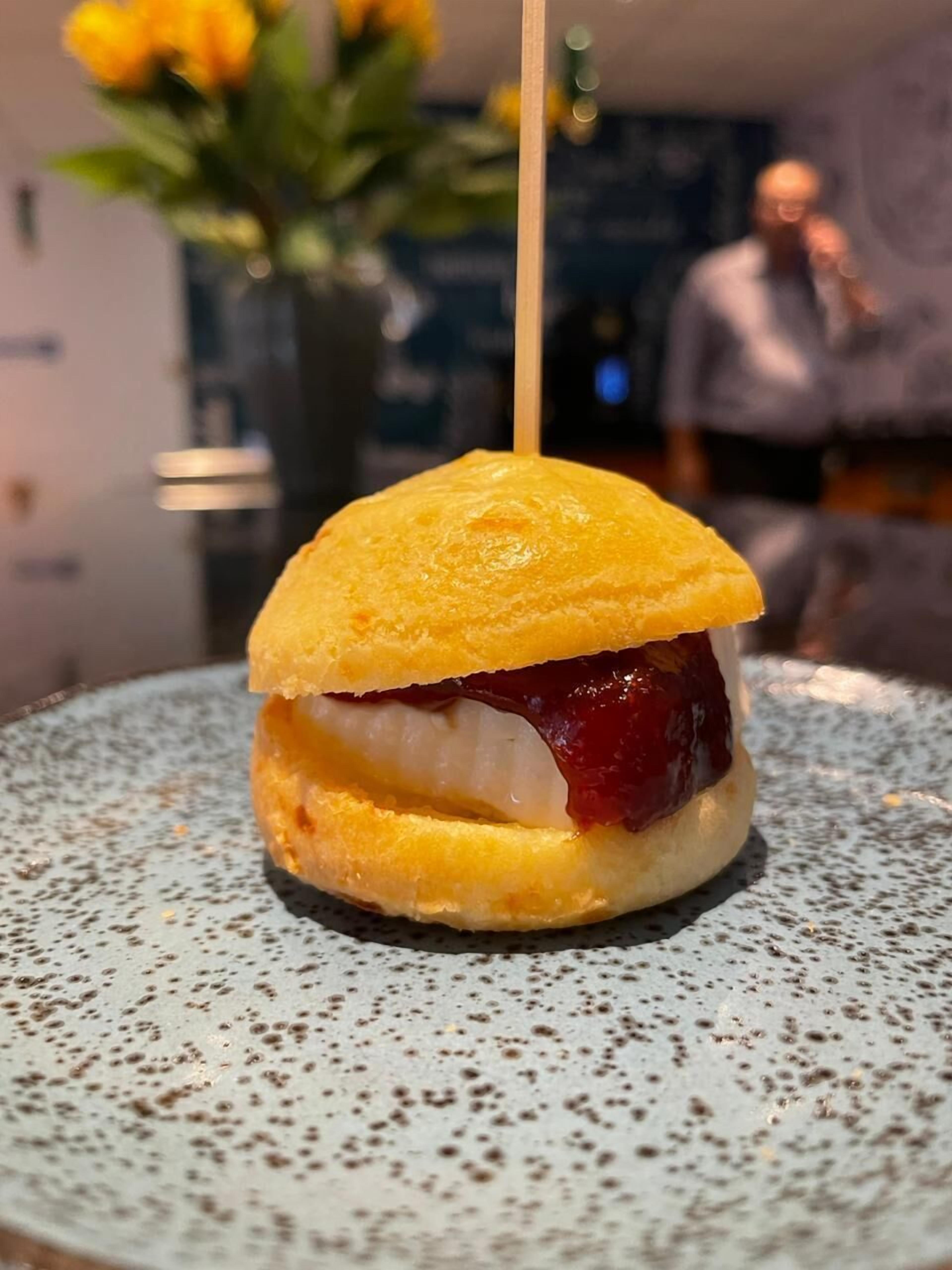 A dessert with a golden-brown bun, a white filling, and a red fruit topping, served on a speckled plate.