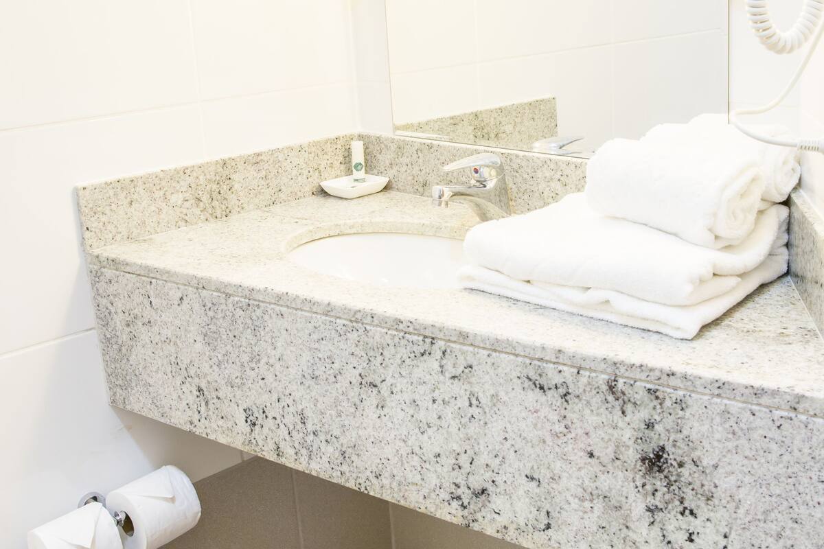 Une salle de bain avec un comptoir en granit, deux miroirs, un sèche-cheveux et une poubelle.