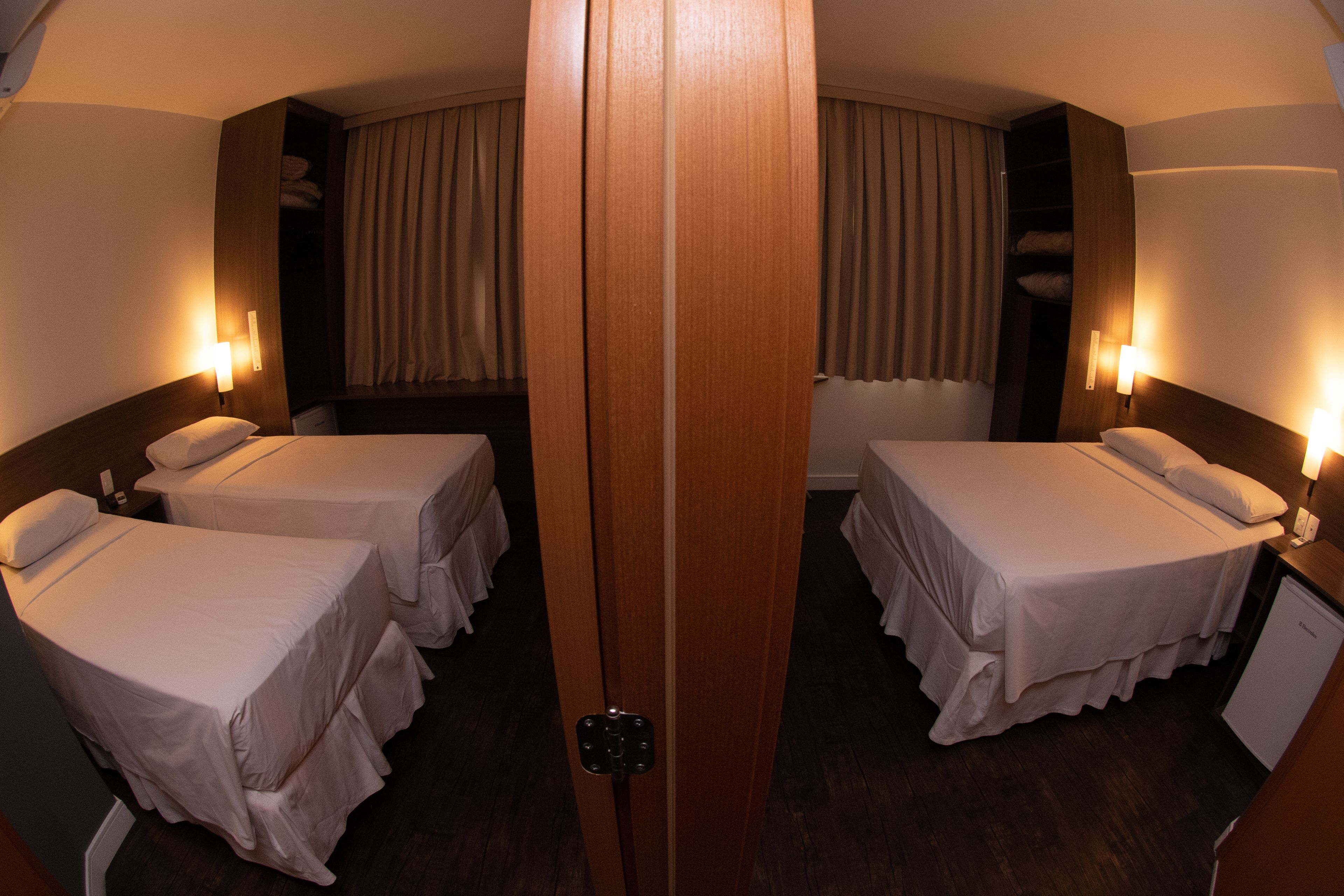 A hotel room with two single beds, a wooden wardrobe, a small desk, and a bathroom with a shower and toilet.