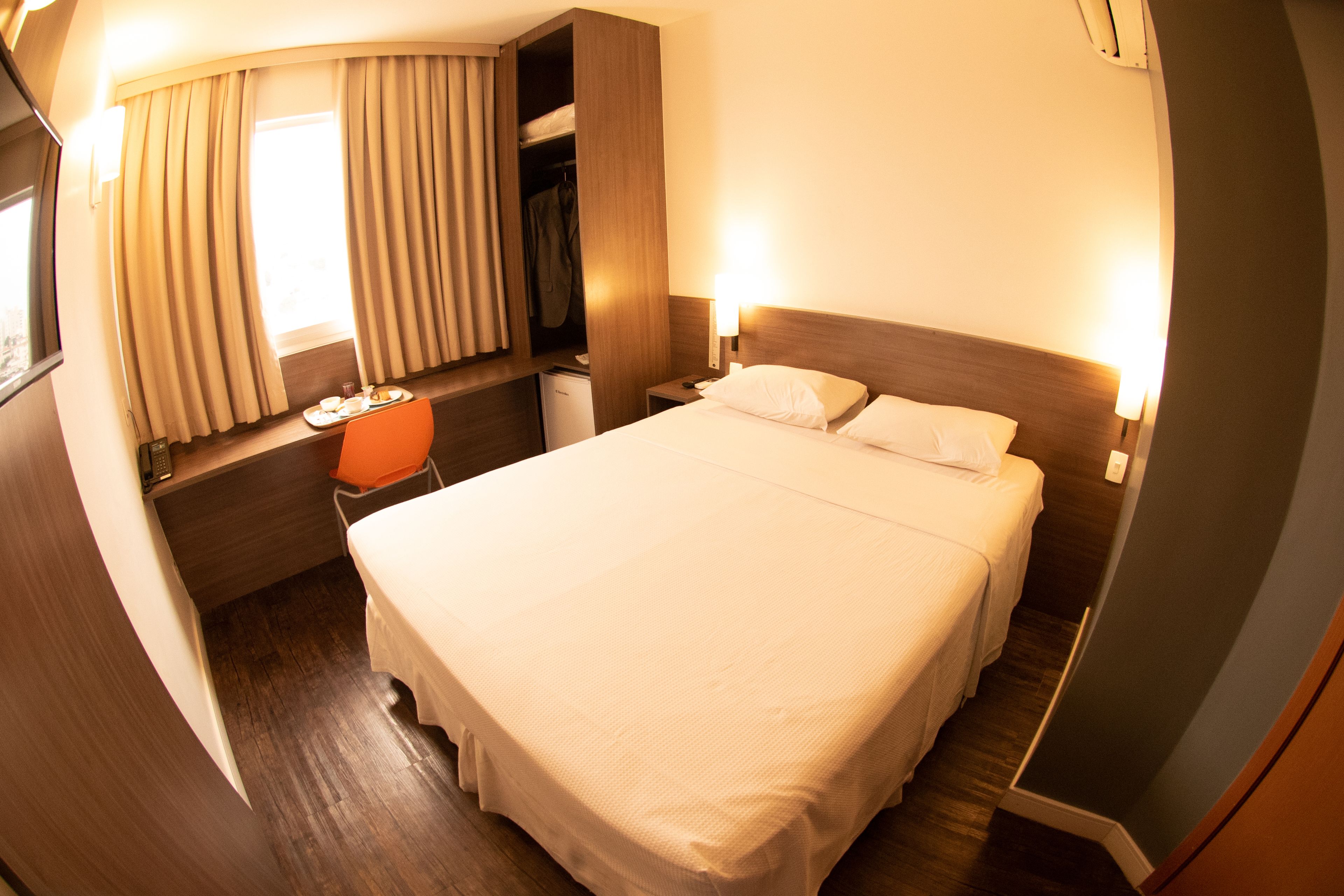 Habitación de hotel con cama, mesitas de noche, escritorio con silla, armario y ventana con cortinas.