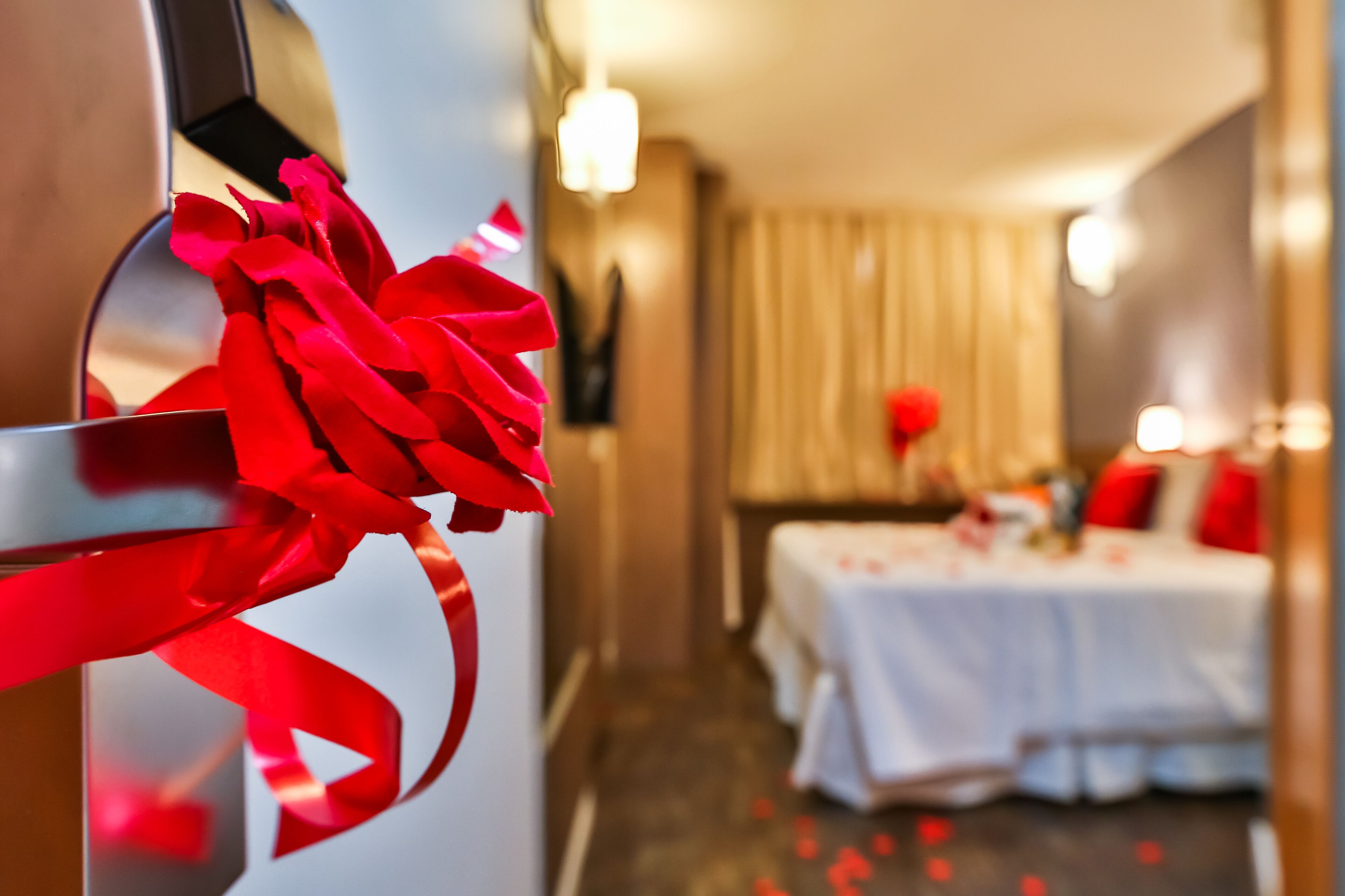 A hotel room with a bed, a white table, and a red bow on the door.