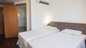 A hotel room with two beds, a wooden door, a glass shower enclosure, and an air conditioning unit.