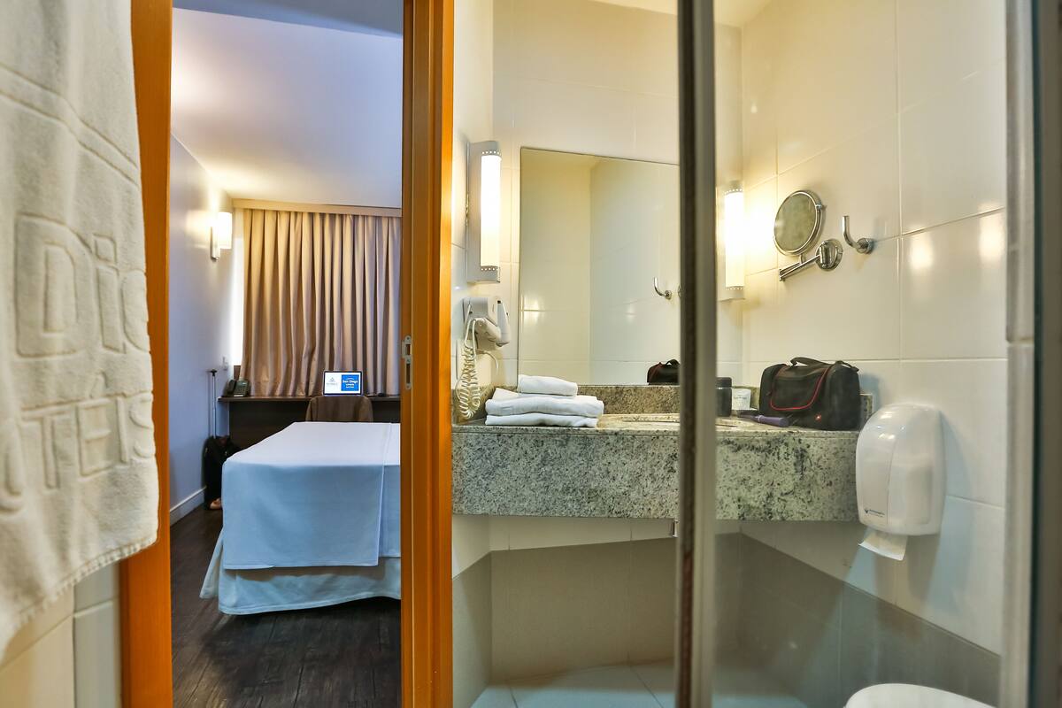 Une chambre d’hôtel comprenant un lit, une salle de bain avec un lavabo, un miroir et des articles de toilette.