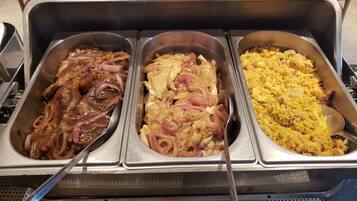 En buffet med tre fade mad: en med glaserede kødretter, en med kylling og løg, og en med ris.