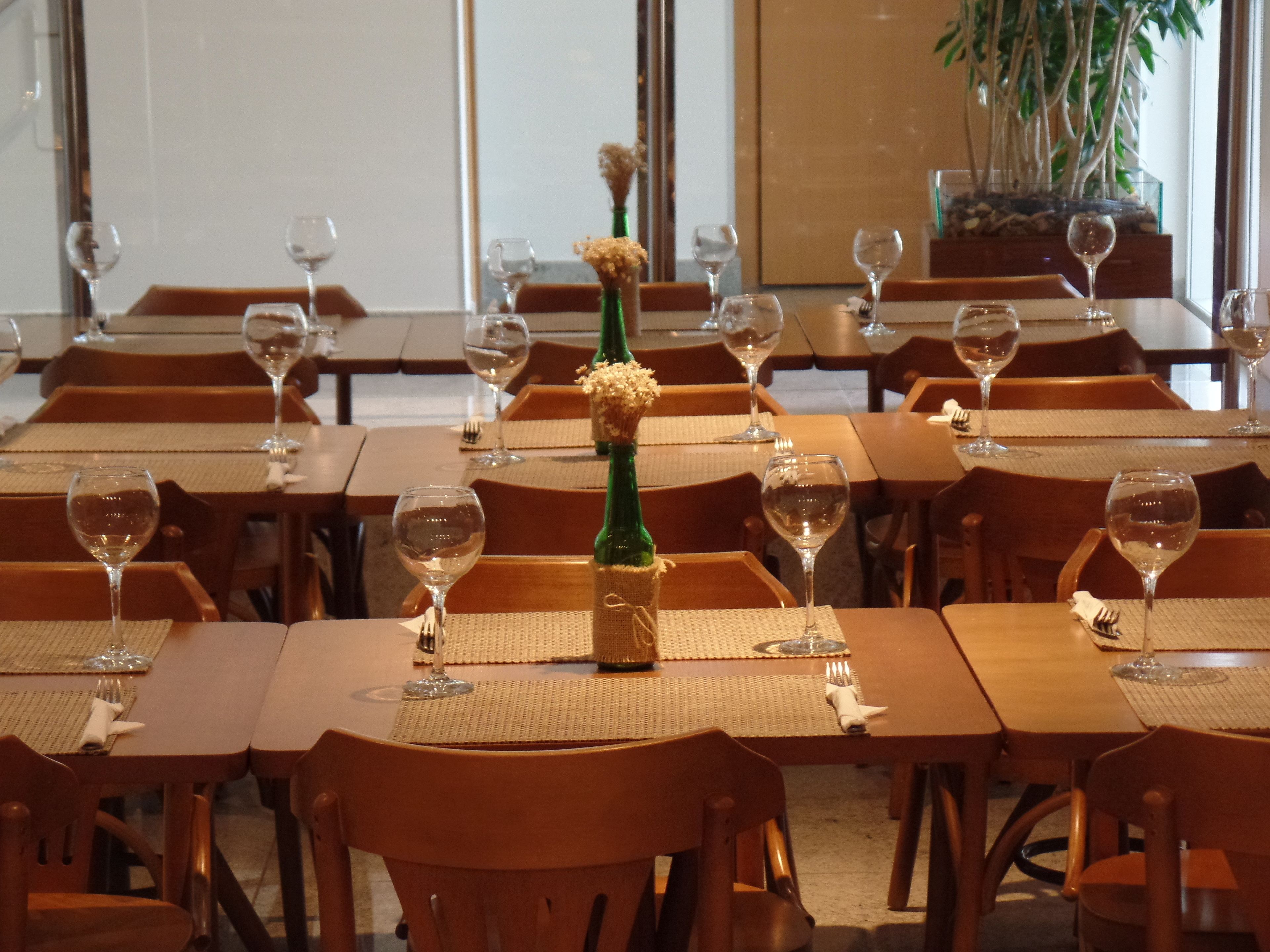 En restaurant med flere borde, hvor hvert bord er dækket med et vinglas, en vinflaske og en lille vase med blomster.