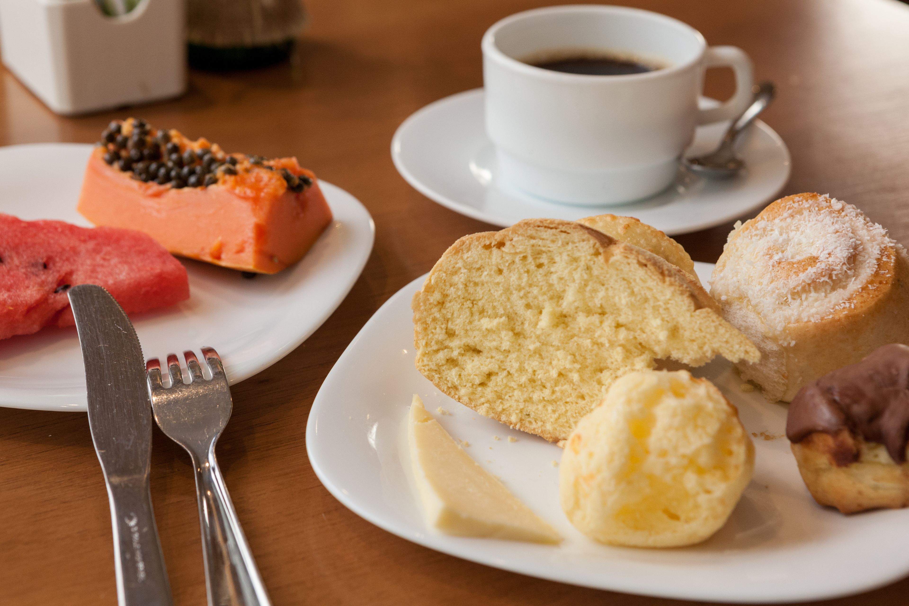 Una mesa con platos de comida que incluyen una rebanada de sandía, un trozo de pastel y una galleta, además de una taza de café.