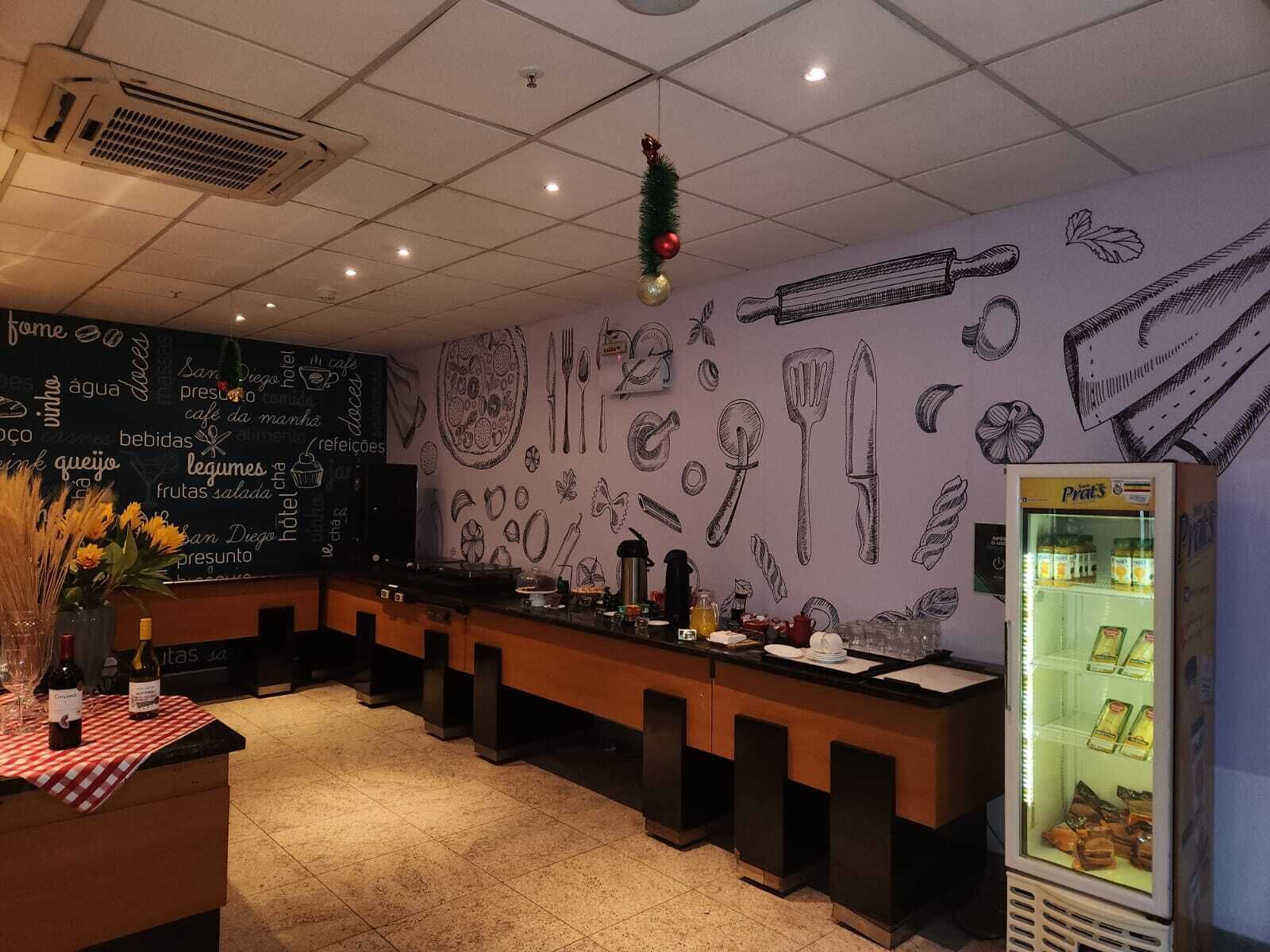 A restaurant with a chalkboard menu, a refrigerator, and a wall decorated with food illustrations.
